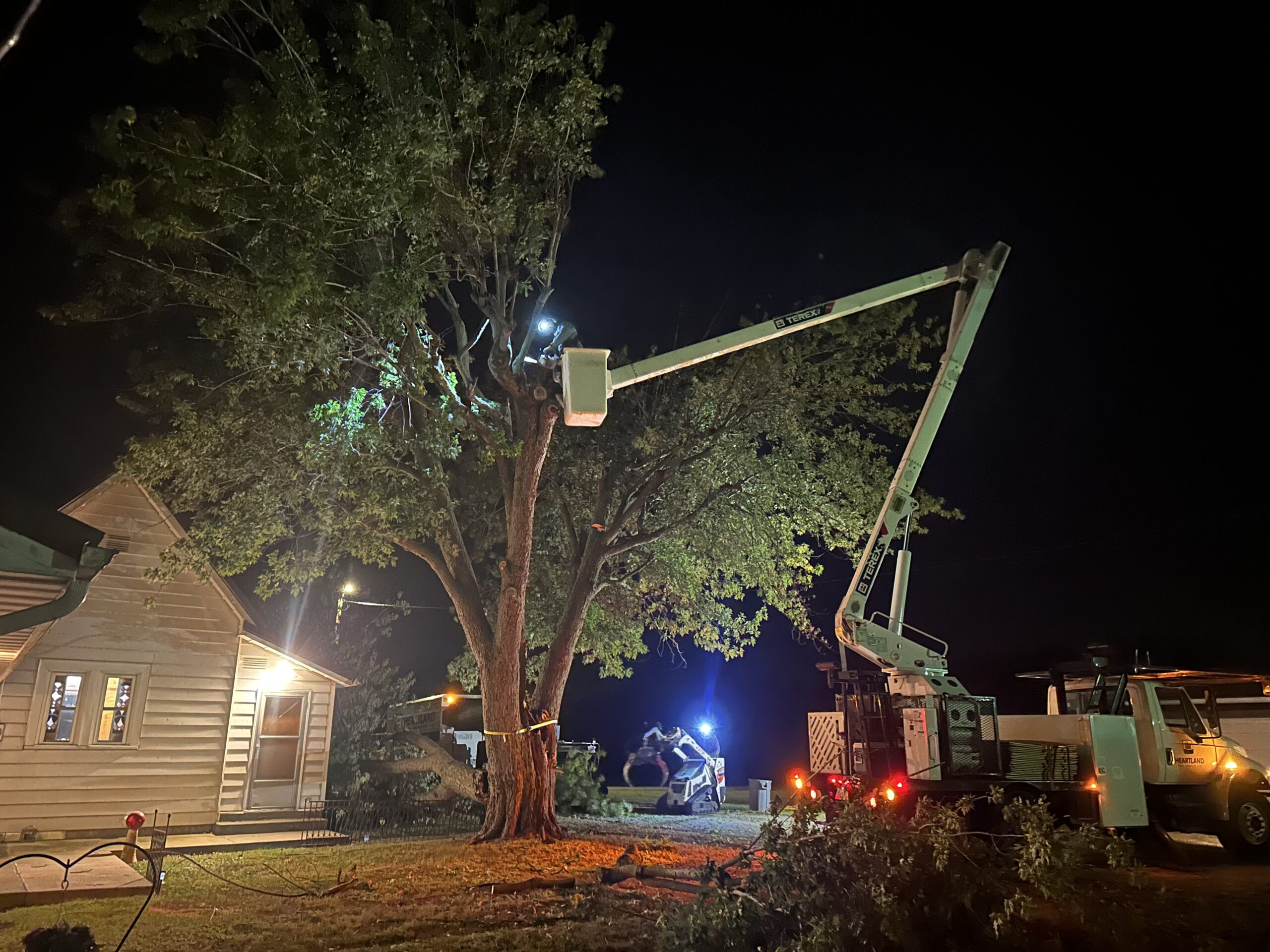 heartland tree service doing an emergency tree service at night with their white bucket truck